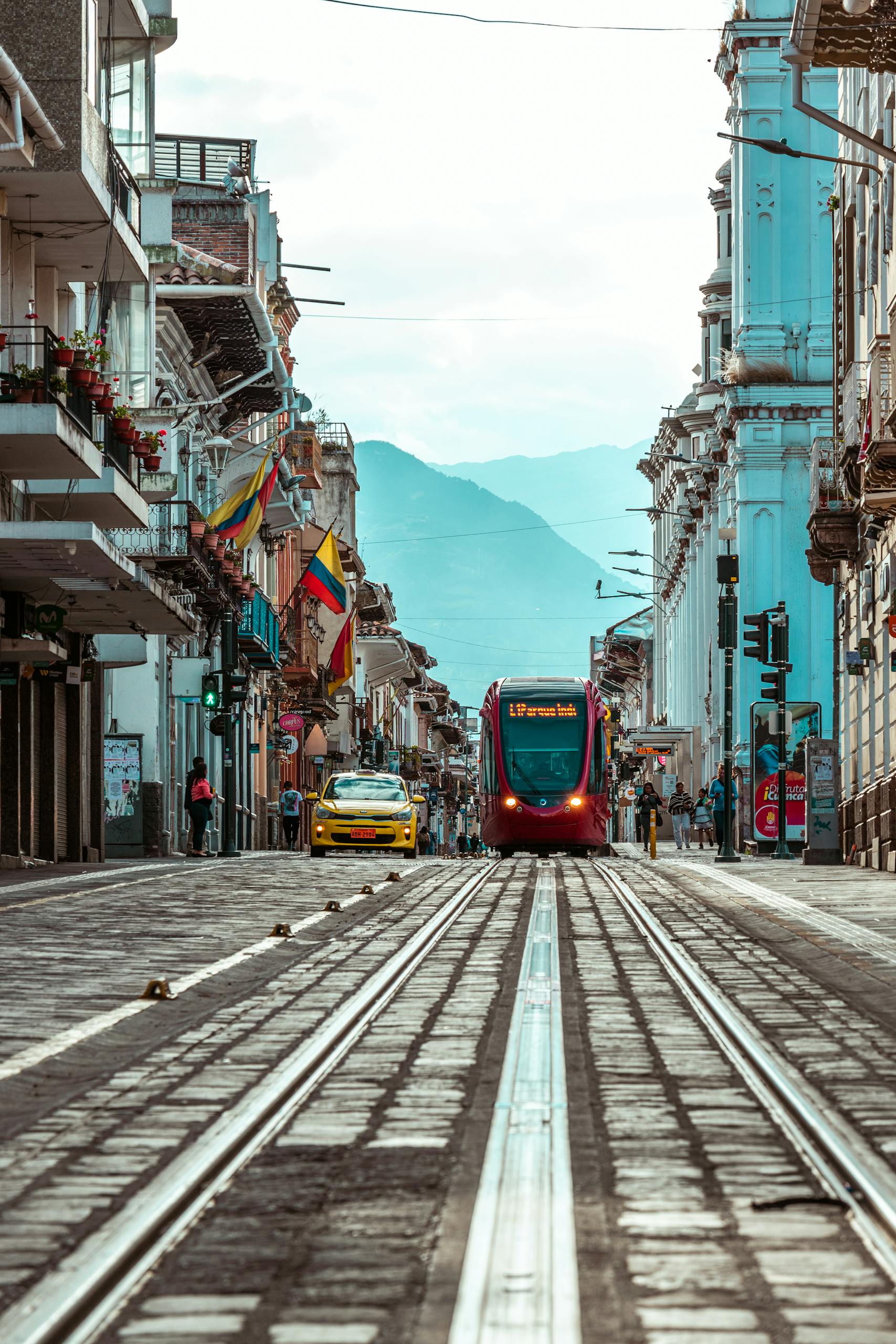 A vibrant street in Cuenca, Ecuador featuring a modern tram and historic architecture under a clear sky.