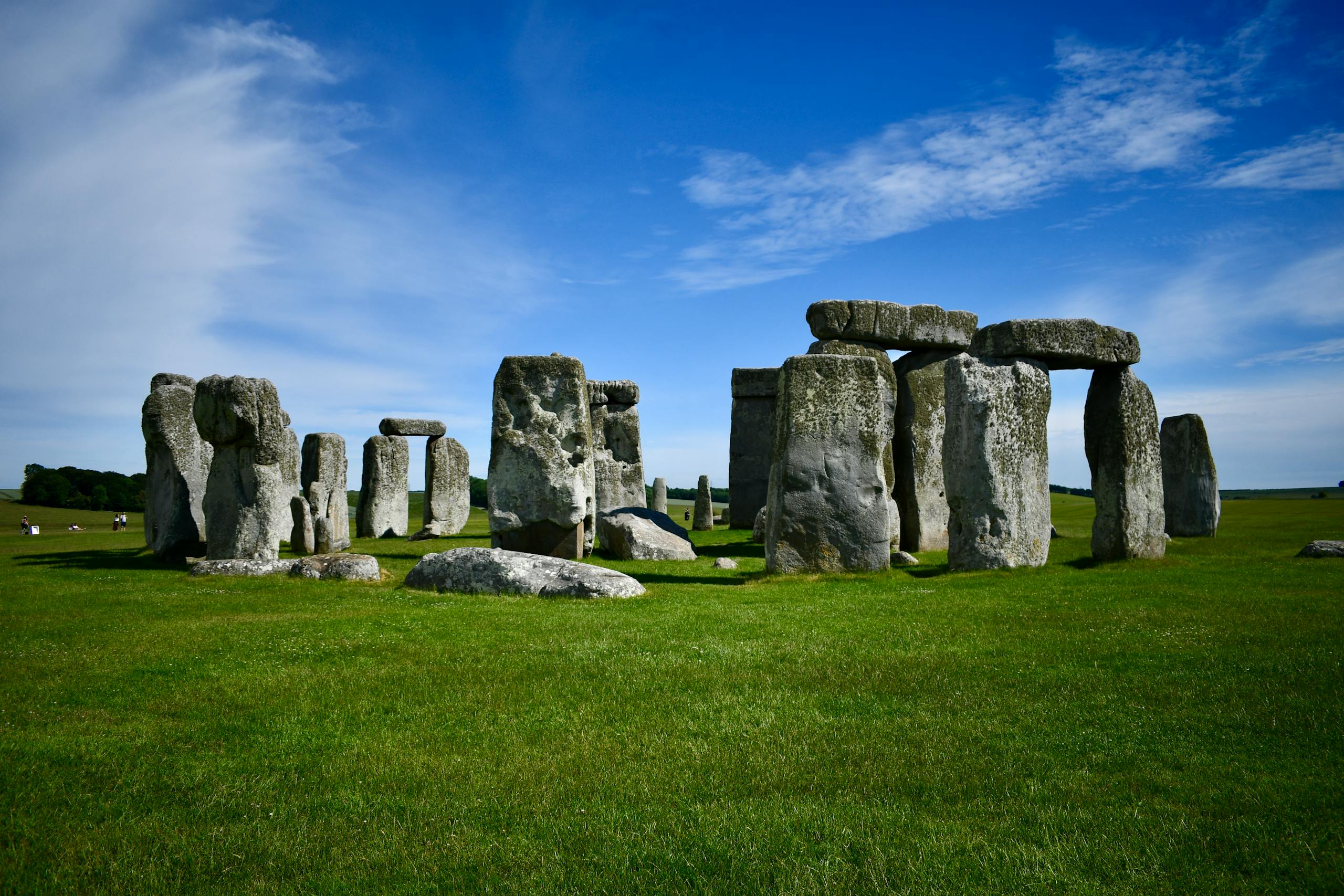 Iconic Stonehenge stones stand tall under a bright blue sky with lush green fields.